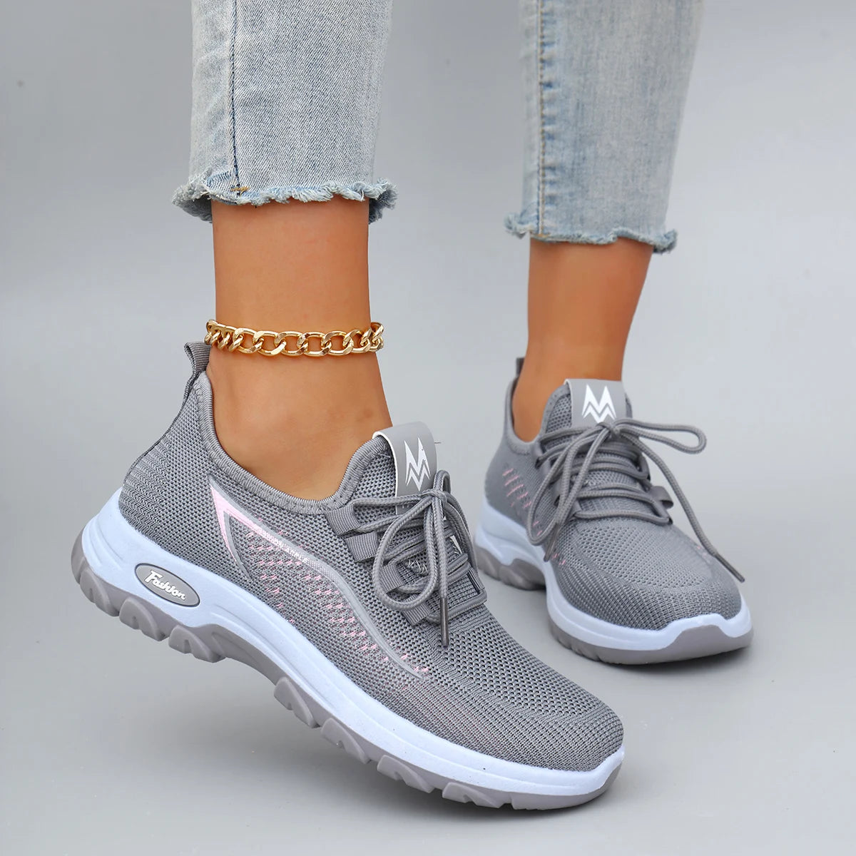 Gray mesh athletic sneakers with white soles and light pink accents worn with frayed jeans.