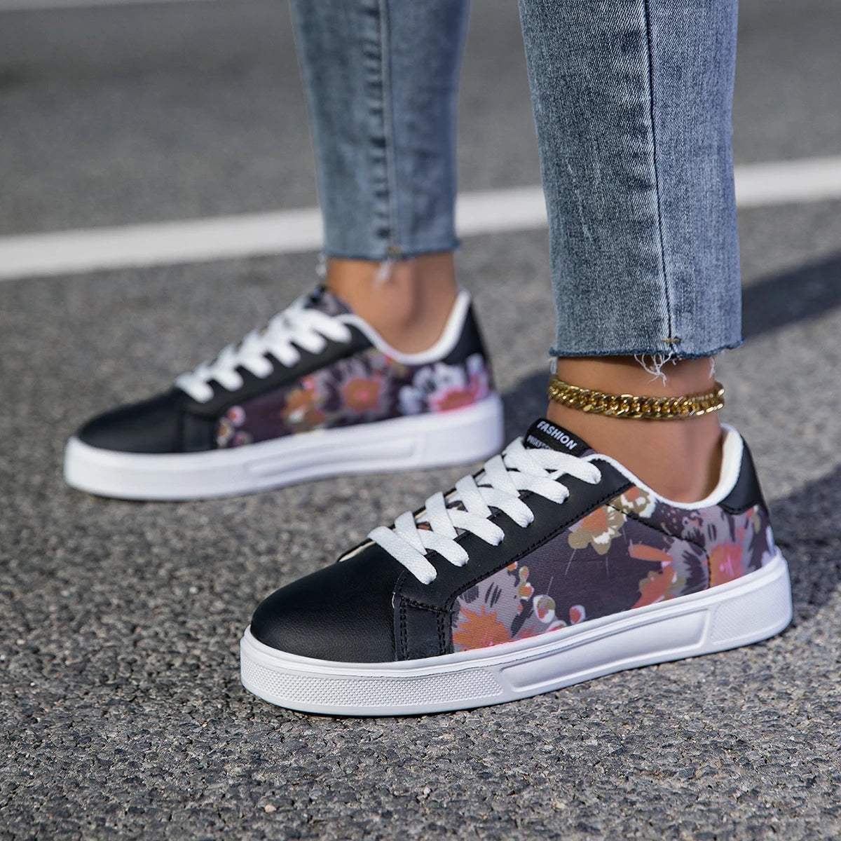 Women’s casual sneakers with black toe cap and colorful abstract floral side pattern, worn with light blue jeans outdoors